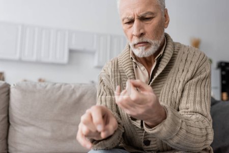 Foto de Worried senior man suffering from parkinsonian syndrome and looking at trembling hands on blurred foreground - Imagen libre de derechos