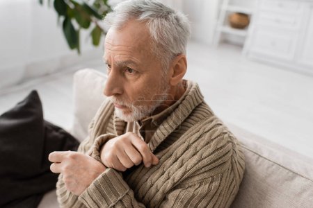 Foto de Depressed man with parkinsonian syndrome and tremor in hands looking away while sitting at home - Imagen libre de derechos