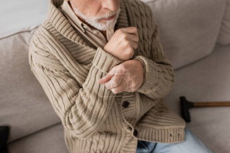 Téléchargez les photos : Cropped view of senior man in knitted cardigan suffering from parkinsonism and tremor in hands while sitting at home - en image libre de droit