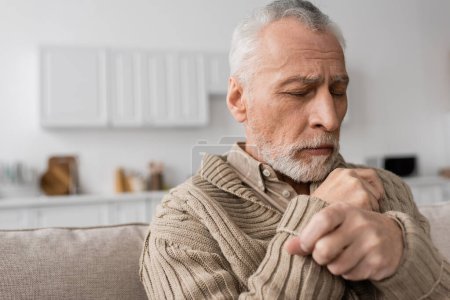 Foto de Depressed senior man with parkinson disease sitting with closed eyes at home - Imagen libre de derechos