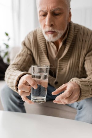 Téléchargez les photos : Blurred man with parkinson syndrome and tremor in hands sitting and holding glass of water at home - en image libre de droit