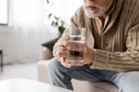 Foto de Partial view of senior man with parkinson disease holding glass of water in trembling hands - Imagen libre de derechos
