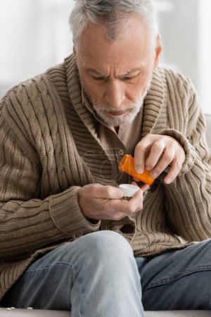 Photo for Grey haired man in knitted cardigan holding pills from parkinson disease in trembling hands - Royalty Free Image
