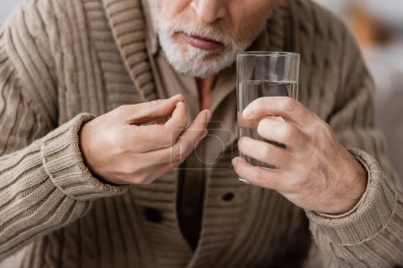 Foto de Partial view of senior man with parkinson disease holding pill and glass of water in trembling hands - Imagen libre de derechos
