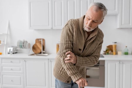 Téléchargez les photos : Grey haired man suffering from parkinsonism and hands tremor standing with walking cane in kitchen at home - en image libre de droit