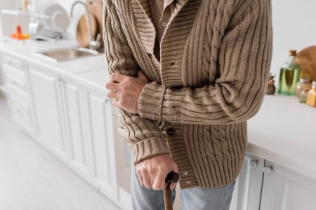partial view of aged man with parkinson syndrome standing with walking cane in kitchen