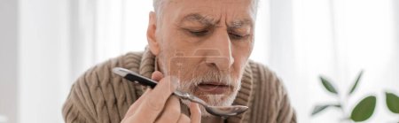 Foto de Senior bearded man suffering from parkinsonism and holding spoon while having dinner in kitchen, banner - Imagen libre de derechos