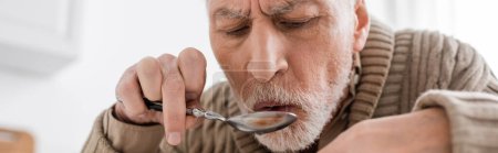 bearded senior man with parkinsonian syndrome and hands tremor holding spoon while having dinner at home, banner