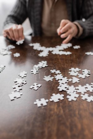 selective focus of jigsaw puzzle elements near cropped man with parkinson syndrome on blurred background