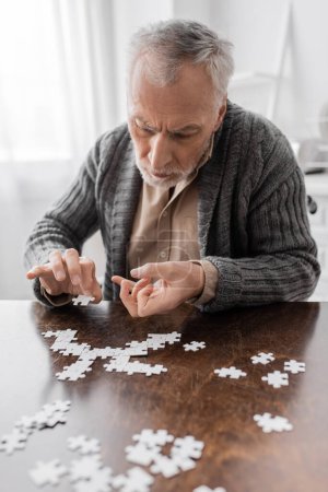 aged man with parkinsonian syndrome and tremor in hands combining jigsaw puzzle on table at home