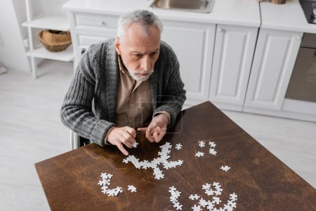 high angle view of grey haired man with parkinsonian syndrome combining jigsaw puzzle on kitchen at home