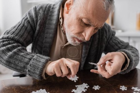 Foto de Senior man with trembling hands caused by parkinson disease combining jigsaw puzzle at home - Imagen libre de derechos