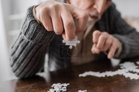 Foto de Partial view of blurred man with parkinson syndrome holding element of jigsaw puzzle in trembling hand - Imagen libre de derechos