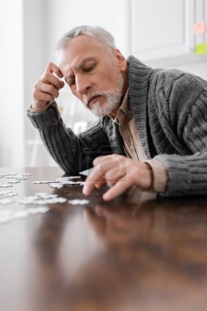 aged man with parkinson disease and trembling hands combining jigsaw puzzle on blurred foreground