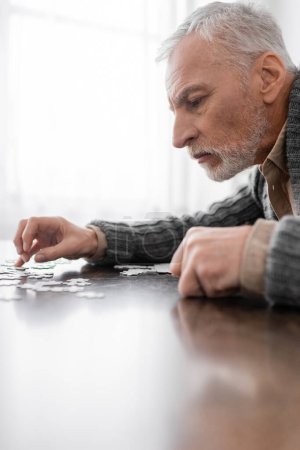 Photo for Side view of aged man with parkinson syndrome combining jigsaw puzzle at home - Royalty Free Image