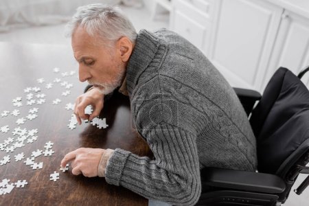 high angle view of man with parkinson disease sitting in wheelchair near elements of jigsaw puzzle