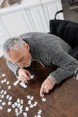 high angle view of man with disability caused by parkinson disease sitting in wheelchair and combining jigsaw puzzle