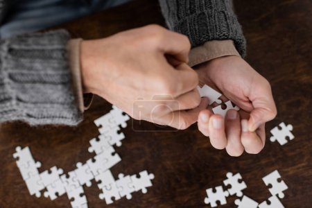 Foto de Cropped view of senior man suffering from parkinsonism and holding elements of jigsaw puzzle in trembling hands - Imagen libre de derechos