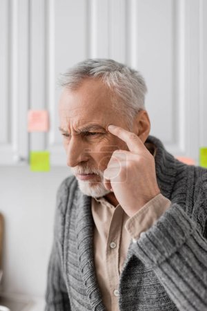 Téléchargez les photos : Tensed man suffering from memory loss and touching head while thinking near blurred sticky notes in kitchen - en image libre de droit