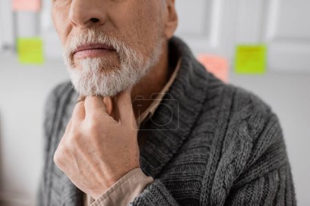 cropped view of aged man with alzheimer syndrome thinking and touching beard in kitchen