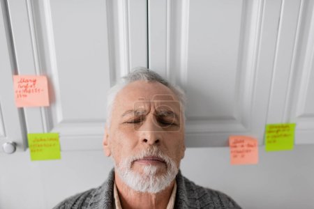 Foto de Depressed man suffering from azheimers syndrome standing with closed eyes in kitchen - Imagen libre de derechos