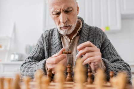 Foto de Tensed man with alzheimer syndrome looking at chess figure near chessboard on blurred foreground - Imagen libre de derechos