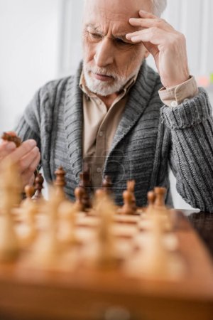 thoughtful senior man suffering from memory loss and looking at chess figure on blurred foreground