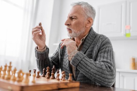 Téléchargez les photos : Tense man suffering from memory loss and looking at chess figure while sitting at home - en image libre de droit