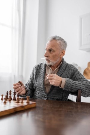 aged man with alzheimer disease holding chess figure and looking away