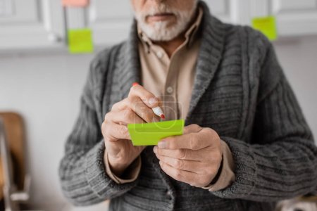 cropped view of aged man with alzheimer disease writing on sticky notes at home