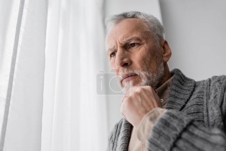 Photo for Tense man suffering from memory loss caused by alzheimer disease standing with hand near chin at home - Royalty Free Image