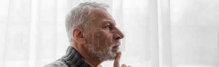 Foto de Profile of senior grey haired man with alzheimer disease touching chin while thinking at home, banner - Imagen libre de derechos