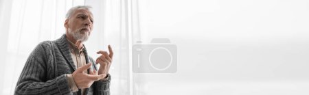 Foto de Aged man with alzheimer syndrome gesturing near window at home, banner - Imagen libre de derechos