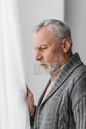 Photo for Side view of depressed senior man with alzheimer diseased looking away near window at home - Royalty Free Image