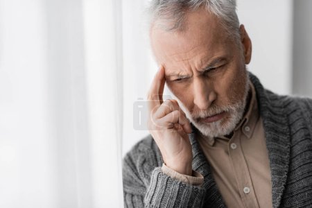 Téléchargez les photos : Grey haired man suffering from memory loss and alzheimer disease touching forehead while thinking at home - en image libre de droit