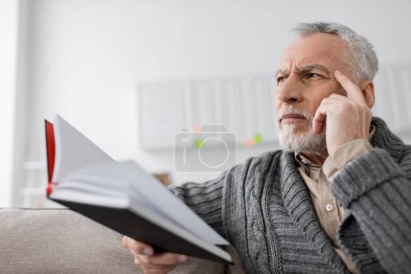 Téléchargez les photos : Tense man with alzheimer syndrome touching head and looking away while holding blurred notebook - en image libre de droit