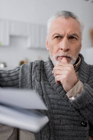 Foto de Aged man with alzheimer disease looking away and thinking near blurred notepad - Imagen libre de derechos