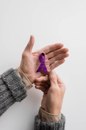 top view of cropped senior man with alzheimer disease holding purple awareness ribbon on white background