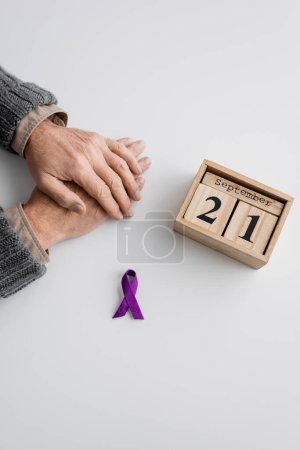 Foto de Top view of purple ribbon and wooden calendar with september 21 date near cropped man with alzheimer syndrome on white surface - Imagen libre de derechos