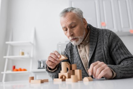 bearded senior man suffering from alzheimer disease and playing building blocks game on table at home
