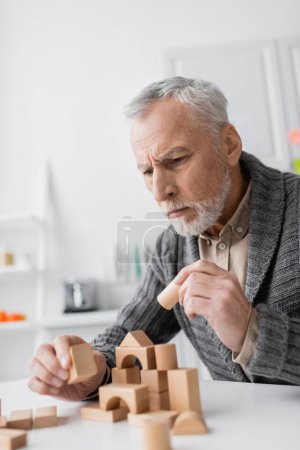 tense man with alzheimer syndrome holding wooden block while playing therapy game at home