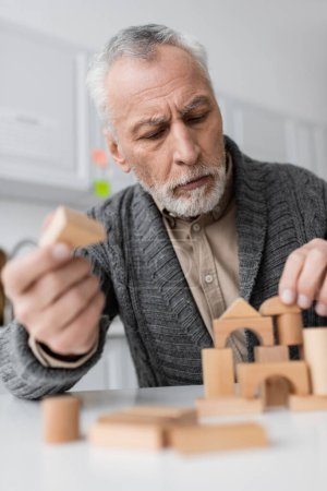 grey haired man in knitted cardigan playing building blocks game while suffering from alzheimer syndrome