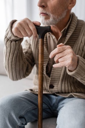 Photo for Cropped view of aged man with parkinson syndrome and hands tremor sitting with walking cane at home - Royalty Free Image