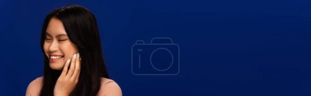 Téléchargez les photos : Brunette asian woman closing eyes and smiling isolated on blue, banner - en image libre de droit