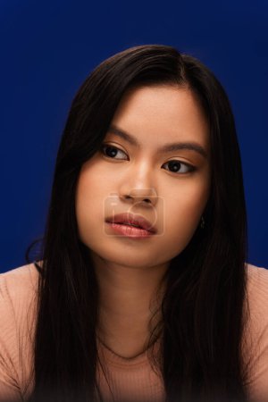 Portrait of young asian woman with natural makeup looking away isolated on blue 