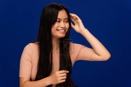 Pretty asian woman with long hair standing isolated on blue 