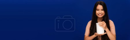 Foto de Young asian woman holding jar with cosmetic product isolated on blue, banner - Imagen libre de derechos