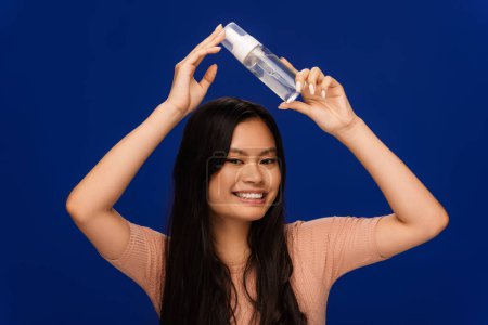 Brunette asian model holding bottle of face cleanser isolated on blue 