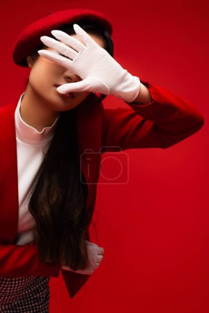 Foto de Trendy model in white glove and beret covering face isolated on red - Imagen libre de derechos
