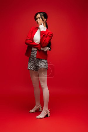 Brunette asian woman with makeup posing while standing on red background 